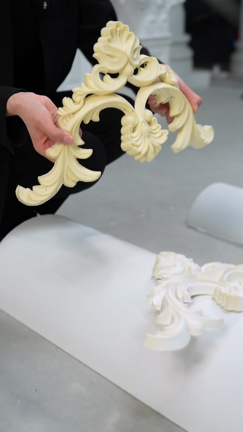 Primo piano di mani che tengono un pezzo curvo di modanatura ornamentale color crema