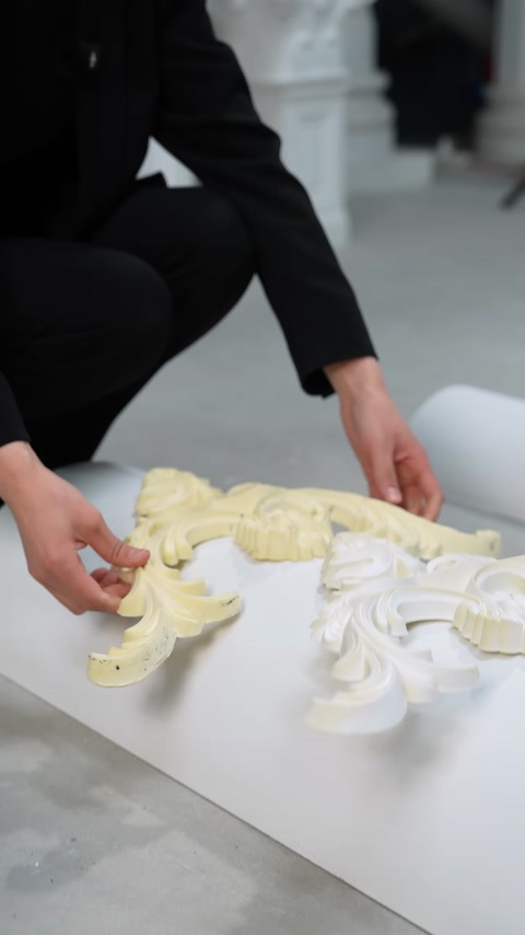 Mani che dispongono pezzi di modanatura color crema e bianca su una superficie curva