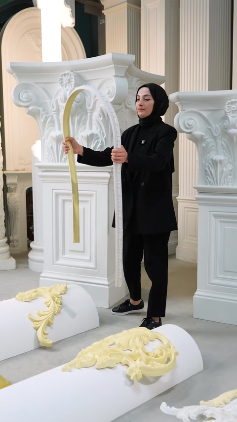 Donna in piedi che tiene una modanatura flessibile color crema curva accanto a colonne
