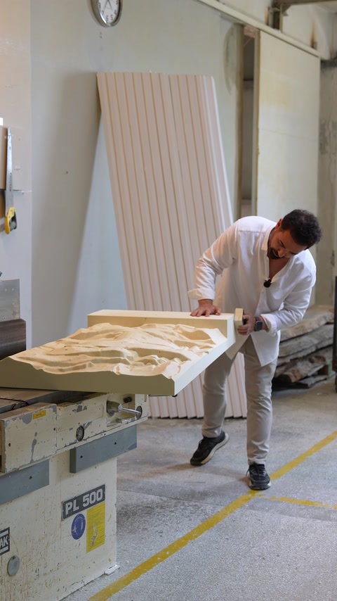 Un artigiano trasporta con attenzione il grande pannello a rilievo nell'area di produzione