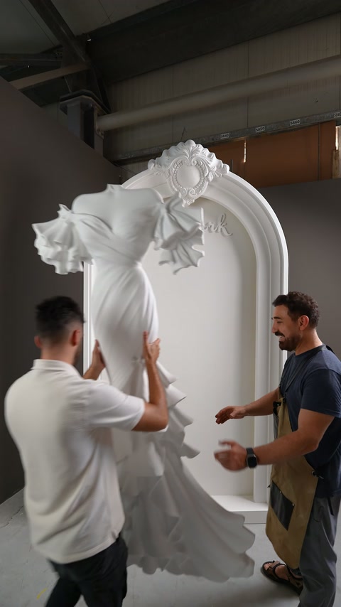 Gli artigiani trasportano il rilievo voluminoso dell'abito da sposa davanti al pannello ad arco
