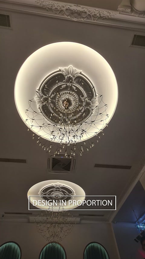 Un elemento circolare illuminato del soffitto circonda un medaglione ornamentale e un lampadario.