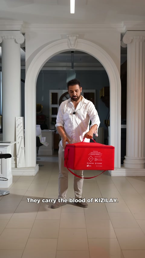 Presenter holds red blood transport case with both hands in front.