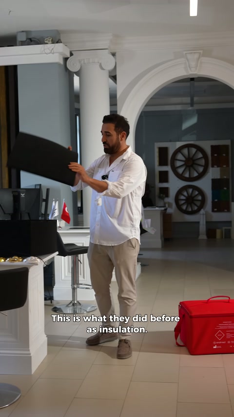 Presenter displays black rectangular insulation panel in showroom.