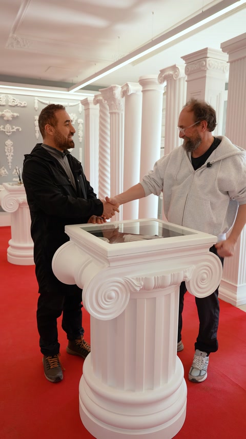 Kubilay Tunçer e il produttore si stringono la mano accanto a una base espositiva di colonne