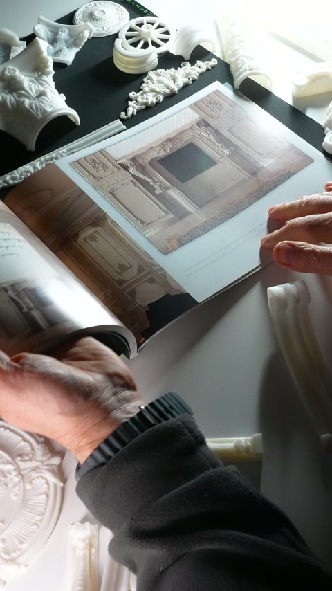 Hands examine a classical interior page beside decorative rosettes and mouldings.