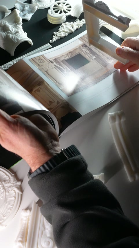 A rectangular moulding sample is held upright above the catalogue.