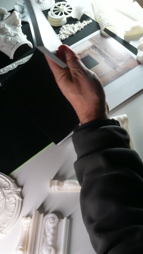 Hands begin closing the catalogue beside white columns and rosettes.