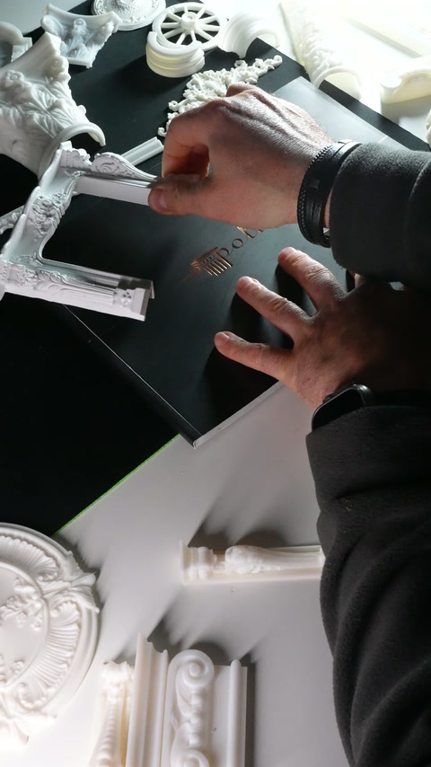 A hand holds carved moulding pieces above column and rosette samples.