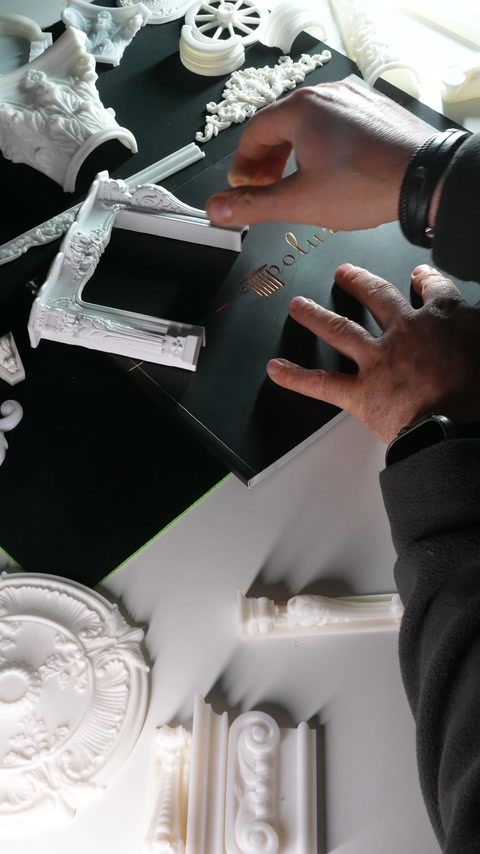 Fingers grip the upper rail of an elaborate miniature frame sample.