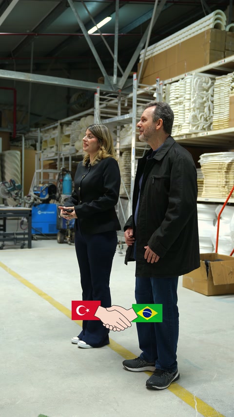 Ziyaretçiler istiflenmiş dekoratif ürünlerin bulunduğu fabrika koridorunda ilerliyor.