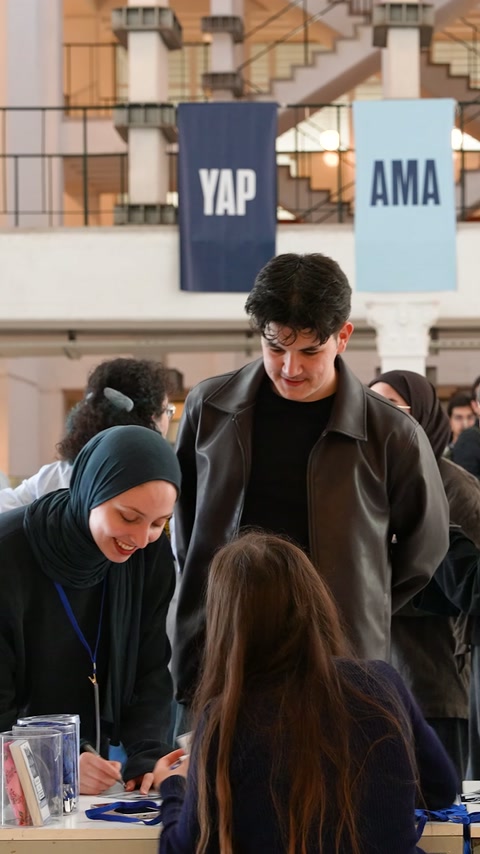 Öğrenciler, afişlerin altındaki kayıt masasında görevlilerle görüşüyor