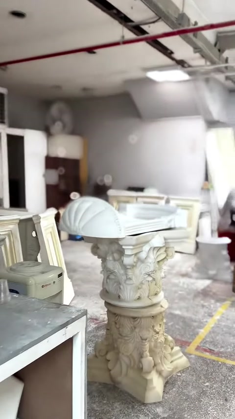 A finished Corinthian capital is displayed in the workshop on a short fluted column.