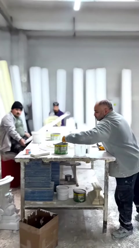 A craftsman works on white decorative pieces at a large production workbench.