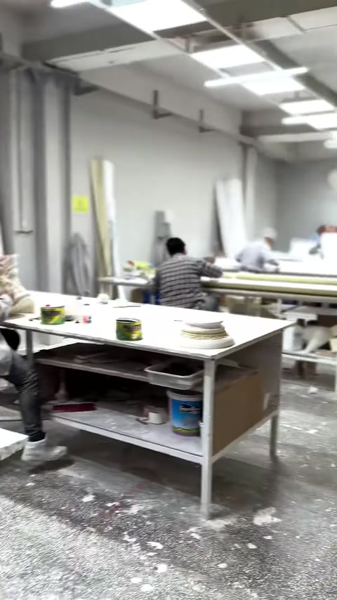 Worktables, columns, and a round decorative ornament are visible in the production workshop.