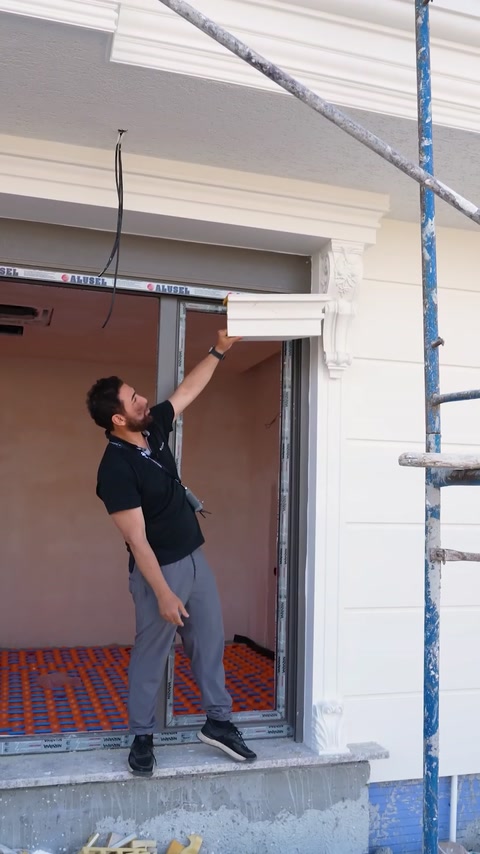 Installer fitting crown molding above window opening on scaffolding