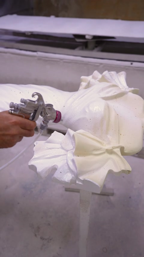 A coating is applied with a spray gun to the curved surface of the wedding dress relief.