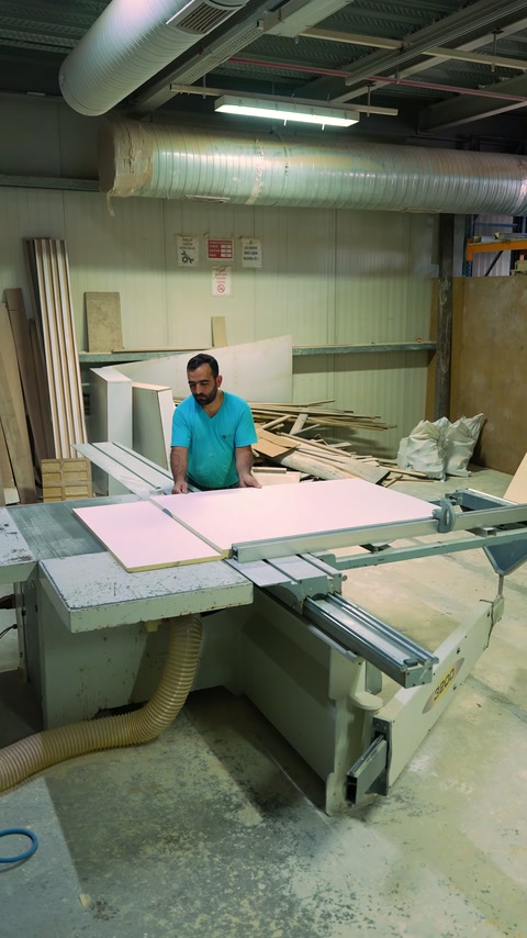 Specialist passes pink board through cutting machine at workshop.