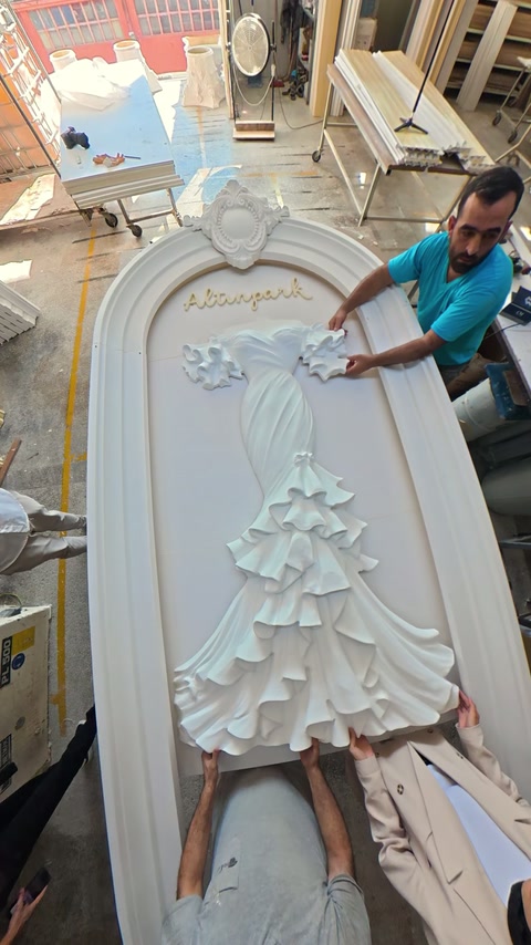 Ornamental relief is carefully positioned at center of curved panel by team.