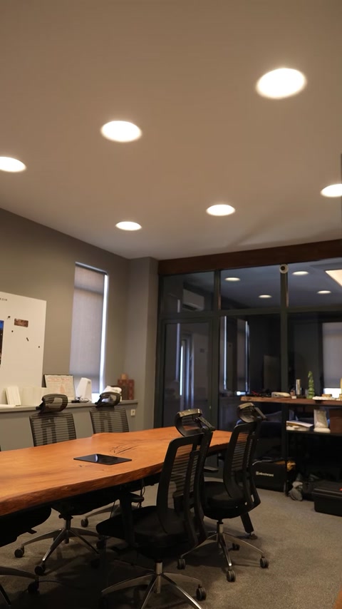 Plafoniere amorfe illuminano una sala riunioni con grandi tavoli da lavoro