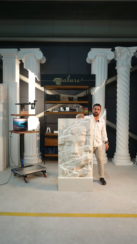 Presenter explains the surface details of a sculptural relief piece standing vertically in the workshop.