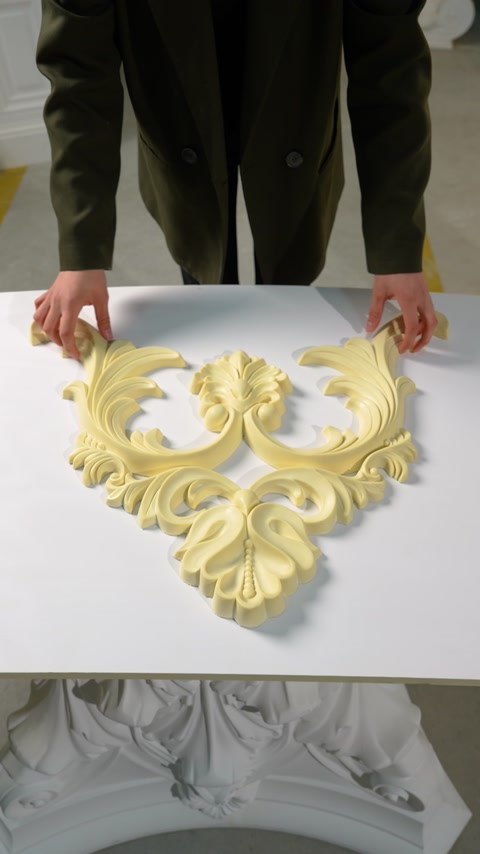 Mani che assemblano elementi di ornamento a volute intagliate su un tavolo bianco