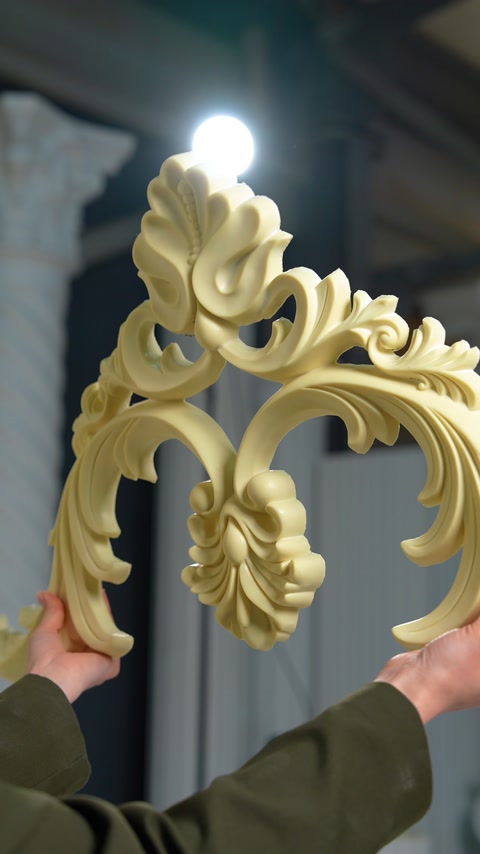 Ornamento a volute d’acanto dettagliato tenuto davanti a una luce da soffitto