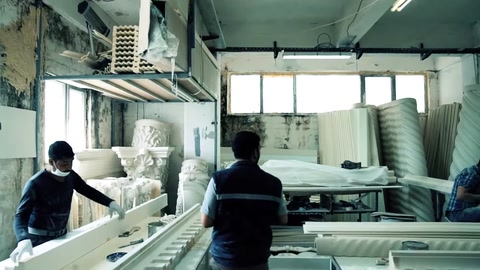 Due operai trasportano insieme un lungo profilo decorativo nell'area di produzione