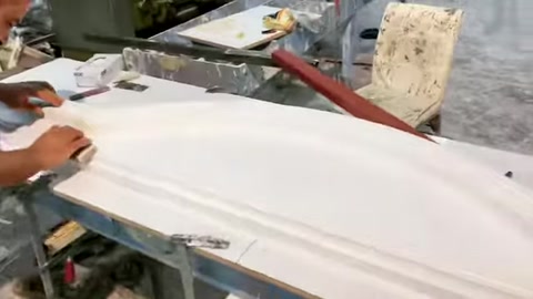 A craftsman works on the surface of a long window surround profile at the bench.