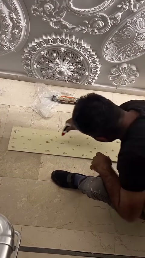 Poliüretan 3D duvar paneli montajında usta arka yüzeye yapıştırıcı sürüyor.