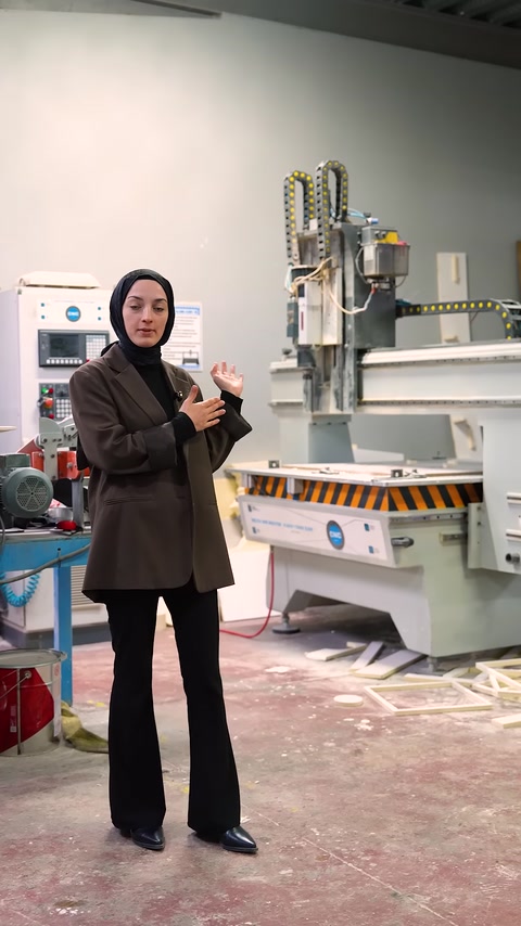 Sunucu, arkasındaki CNC işleme makinesini anlatırken gösteriyor