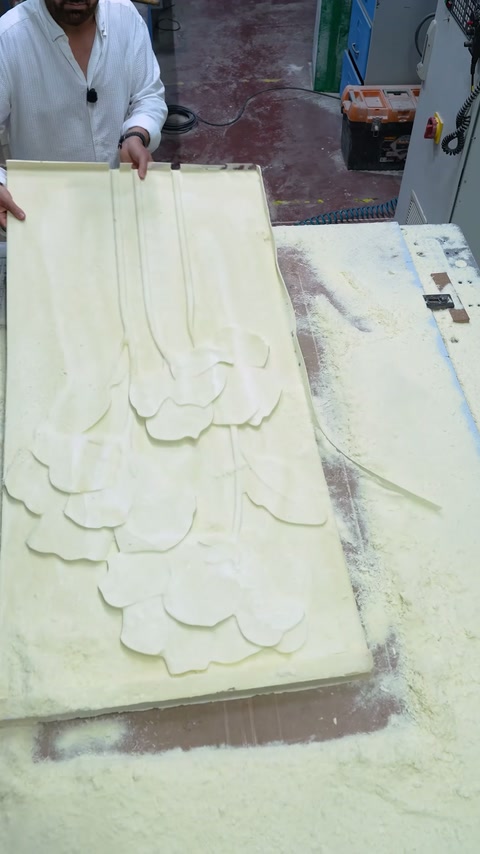 Il pannello lungo a rilievo floreale completato viene tenuto verticalmente sul tavolo CNC.