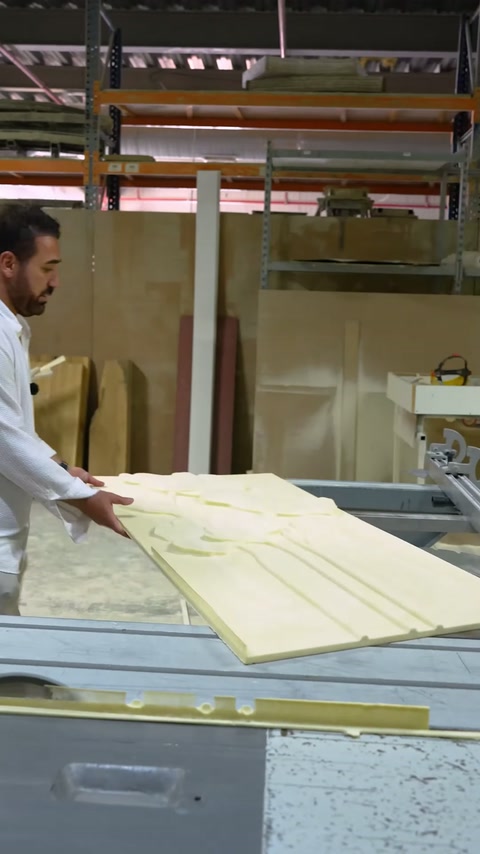 Il maestro artigiano si prepara a sollevare il pannello con motivi floreali dal tavolo della macchina.