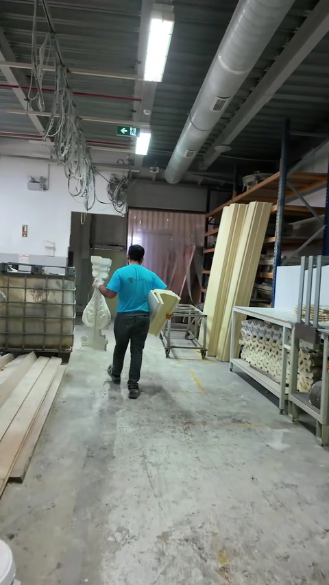 Worker carries an ornate fireplace component across the production workshop.