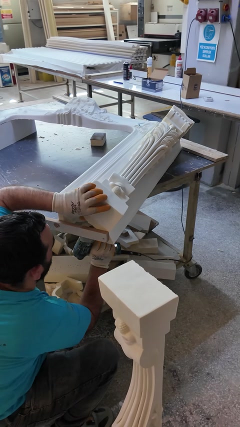 Two workers assemble carved columns and mantel sections on the bench.