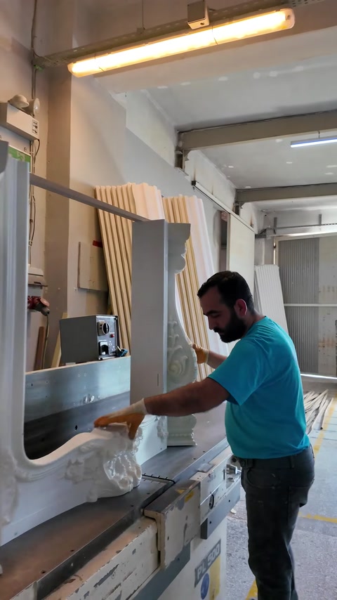 Worker shapes a curved decorative profile using workshop machinery.