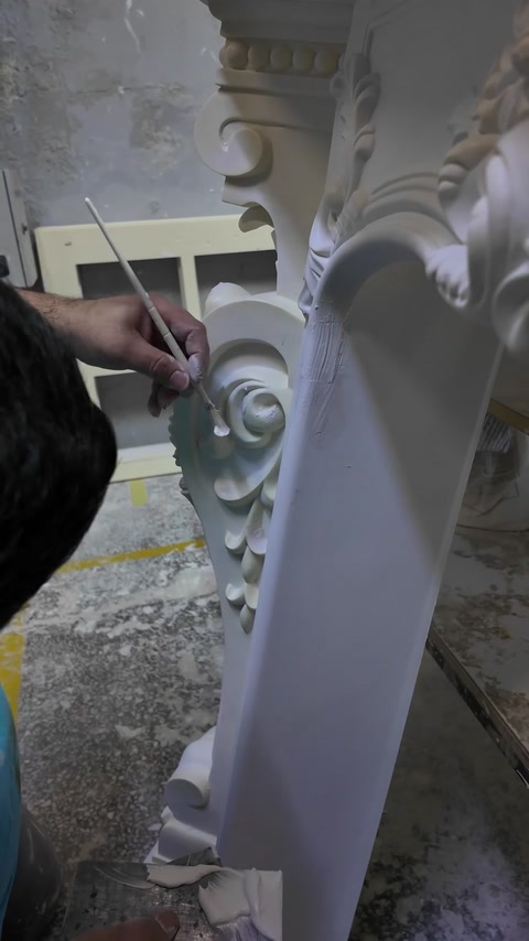 Fine brushwork refines the sculpted scroll on a decorative support.