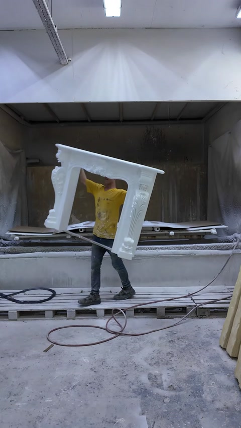 Worker carries the assembled fireplace surround through the finishing booth.