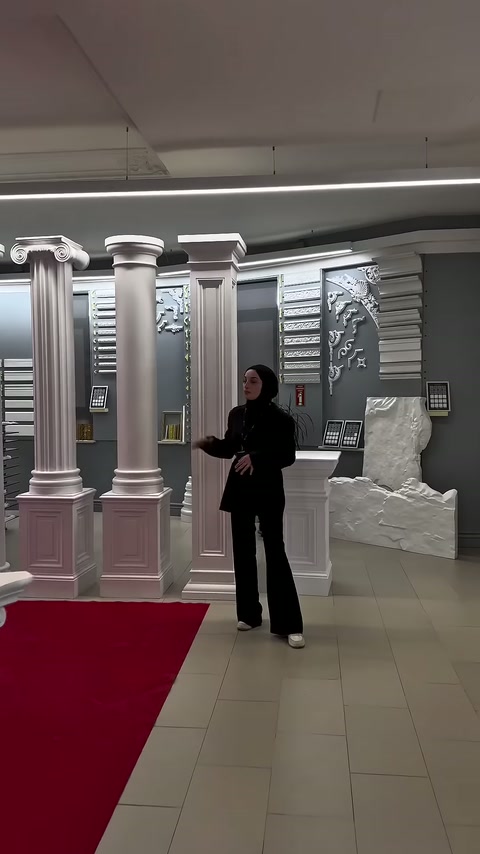 Tanıtıcı, showroomdaki yüksek dekoratif sütun çeşitlerinin önünde duruyor.