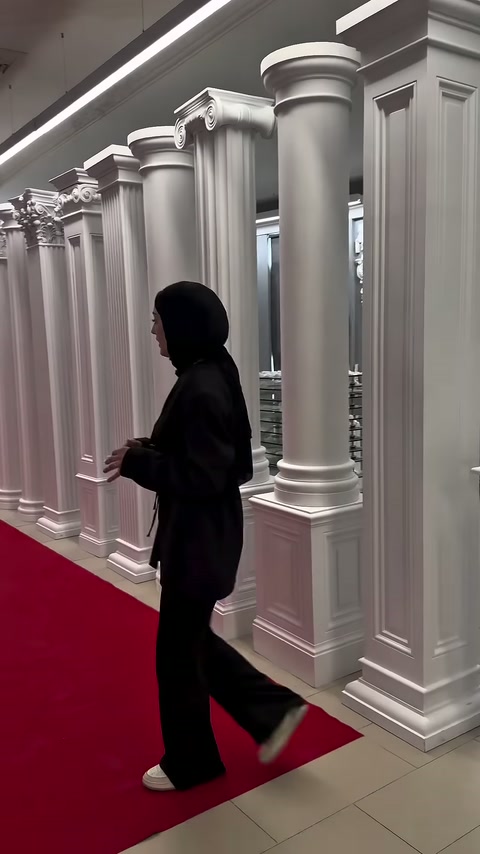 Tanıtıcı, kırmızı halı boyunca dizilen sütunların yanından ilerliyor.