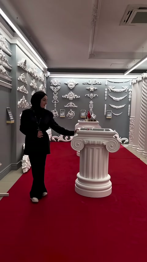 Tanıtıcı, kırmızı halı üzerindeki yuvarlak sütun sehpayı inceliyor.