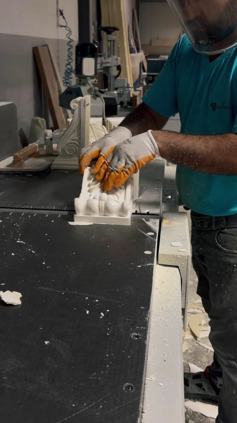 Un operaio con guanti taglia un capitello decorativo con una macchina