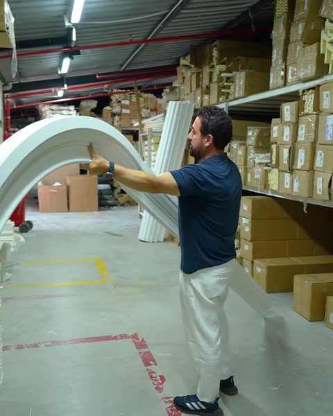 Operaio che trasporta un pezzo di cornice ad arco curvo attraverso l'area di stoccaggio