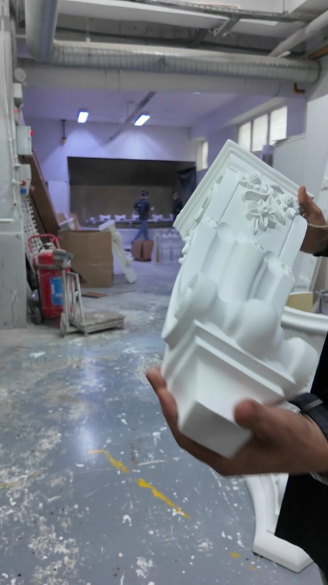 The volute-decorated side of a Corinthian column capital is shown by hand