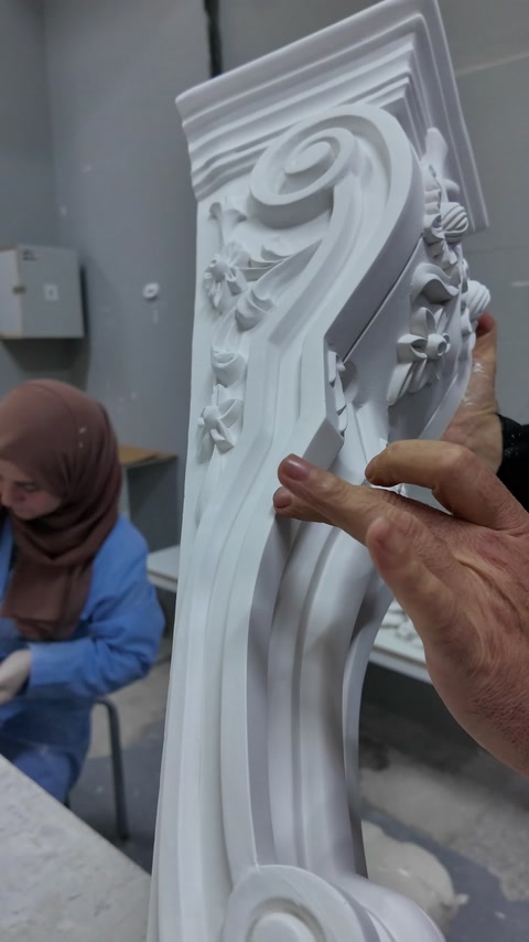 The curved embossing and edge profiles of a long decorative corbel are inspected