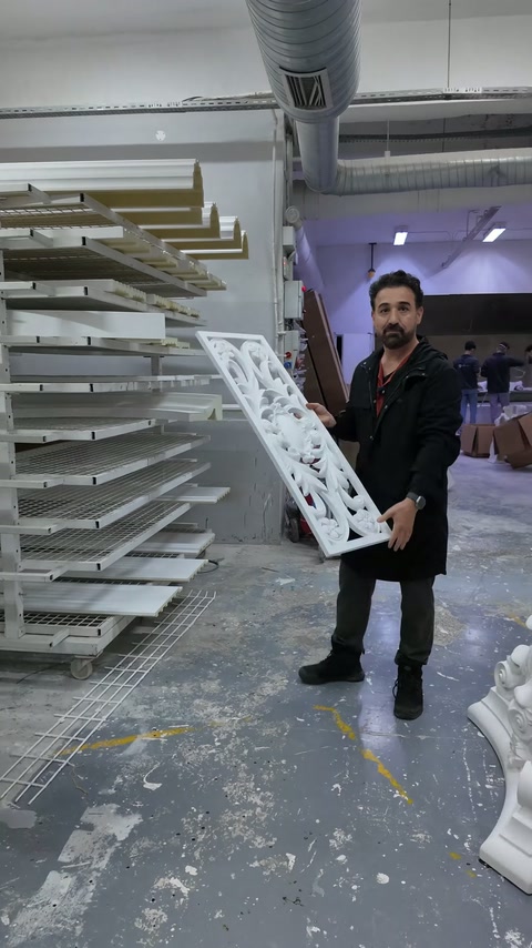 Il maestro trasporta un pannello decorativo traforato davanti agli scaffali di produzione.