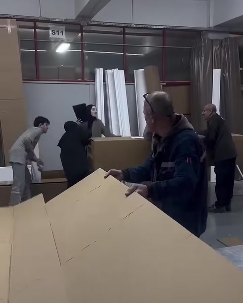 A worker prepares a large cardboard sheet for a packaging box