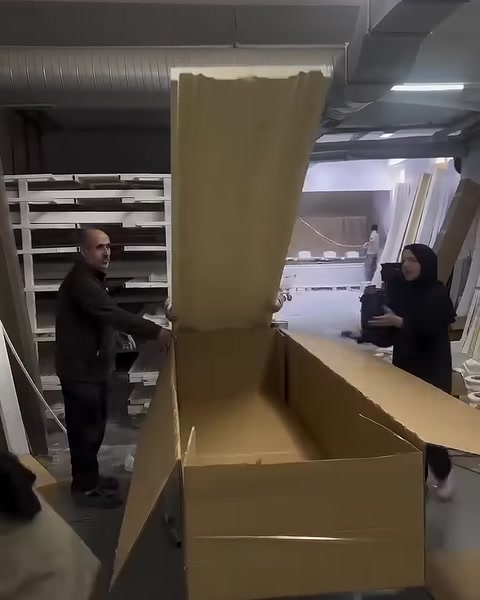 A cut cardboard piece is lifted onto a long product box