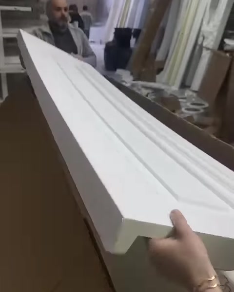 A long grooved cornice molding profile is carefully placed inside a packaging box