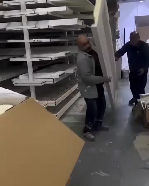 A long white decorative profile is carried in front of the workshop shelves